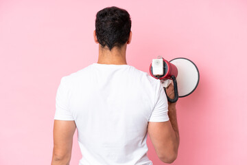 Young caucasian man isolated on pink background holding a megaphone and in back position