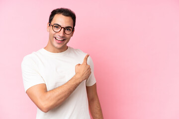 Young caucasian man isolated on pink background surprised and pointing side