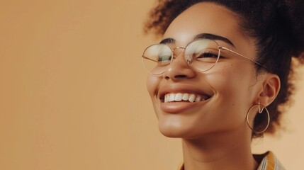 Smiling woman with glasses and curly hair wearing large hoop earrings against a soft-focus beige background.