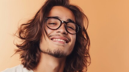 Smiling young man with long hair and glasses against orange background.