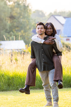This image captures a heartwarming moment between a couple enjoying a piggyback ride. The man, with a content smile, carries the woman, who is embracing him from behind. Both are casually dressed
