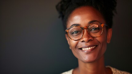 A woman with a warm smile wearing glasses and a light-colored top set against a dark background. - 733776296