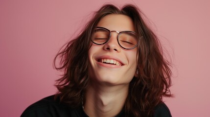 Smiling young person with long hair and glasses against a pink background exuding a sense of joy and carefree youth.