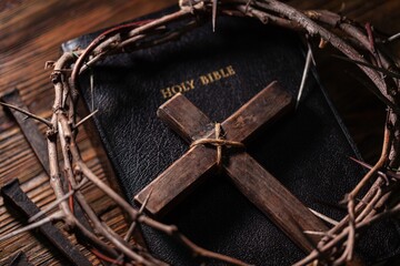 Christian cross with crown thorns and bible on dark desk.