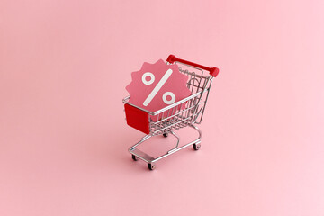 Shopping cart with promotional discount sale icon on pink background - banner image for retail promotion, ecommerce, online sales, coupons and specials with space for text - obrazy, fototapety, plakaty