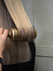 A hairdresser holds a large round comb with a strand of hair twisted onto it.
