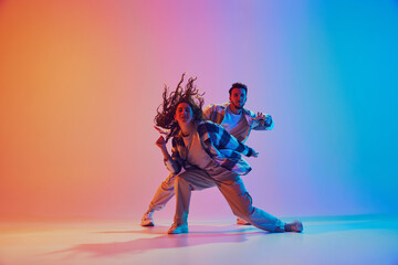 Man and woman dressed in fashionable clothes and dancing in motion to rhythm of music against gradient background. Synchronous movements Concept of movement, energy. Dynamic gel portrait. Ad