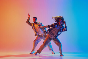 Dynamic shot of athletic man and woman, hip-hop dancers learning new dance routine against gradient...
