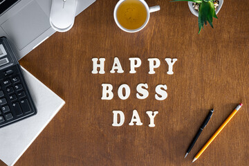 Wooden inscription Happy Boss Day on a wooden office desk background.