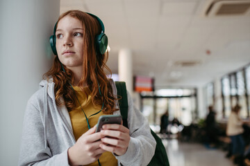 Teenage girl waiting in hospital corridor, listening music. Adolescent patient coming to hospital...