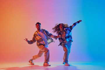 Dancing couple moves in sync, man and woman, dancing in neon-lit studio against gradient background. Energetic expression. Urban style. Concept of movement, energy, dance battles. Dynamic gel portrait