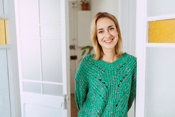 Young beautiful blond woman wearing green sweater, smiling cheerful standing casual at home on a sunny day.