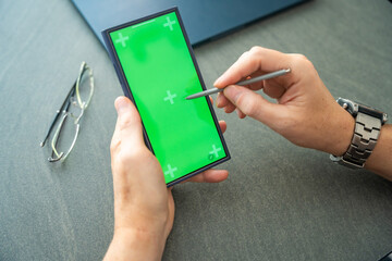 Close up view of man hand holding smart phone with green chroma key screen and stylus pen at his...