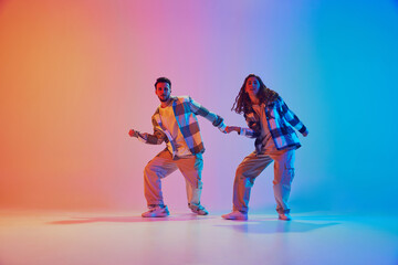 Hip-hop rhythm. Male and female dancers dancing in duet in neon light against gradient studio background. Motion. Concept of movement, energy, dance battles. Dynamic gel portrait