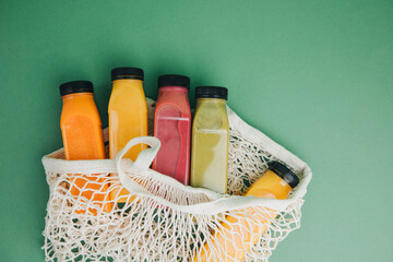 Fruit and vegetable smoothies in transparent plastic bottles in a mesh bag. Red, green, orange smoothies on a green background. The concept of healthy eating. Top view