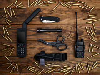 Close-up on a wooden background. Satellite phone with large antenna, radio station, tactical knife,...