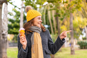 Brunette woman with a cornet ice cream at outdoors pointing to the side to present a product