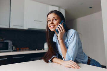 Young woman talking on cell phone while standing in kitchen with microwave oven in background