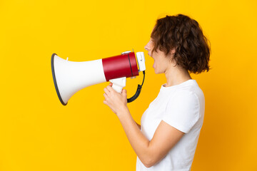 Young English woman isolated on yellow background shouting through a megaphone to announce something in lateral position