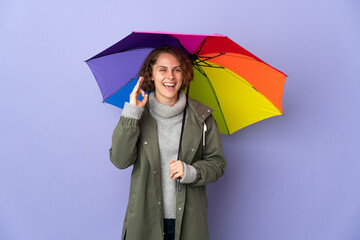 English woman holding an umbrella isolated on purple background showing ok sign with fingers