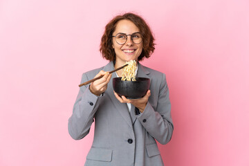 Young English woman isolated on pink background holding a bowl of noodles with chopsticks