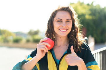 Young sport woman with an apple at outdoors with thumbs up because something good has happened