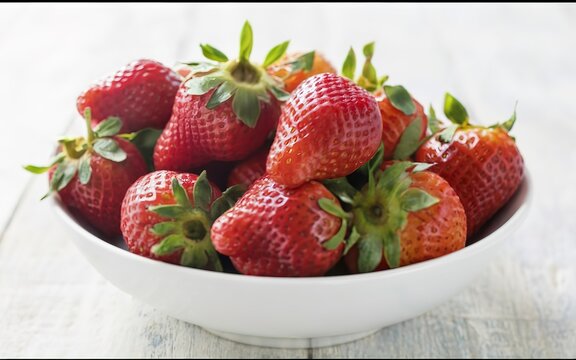Farm fresh ripe red strawberries with attached green stalks served whole in a plain white bowl