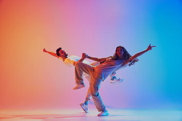 Two talented dancers mid-movement performing in vibrant pink and blue lighting against gradient...
