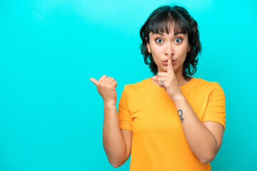 Young Argentinian woman isolated on blue background pointing to the side and doing silence gesture