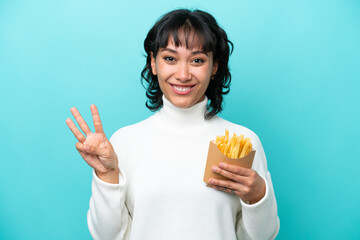 Young Argentinian woman holding fried chips isolated on blue background happy and counting three with fingers