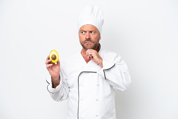 Chef man holding an avocado isolated on white background having doubts and thinking