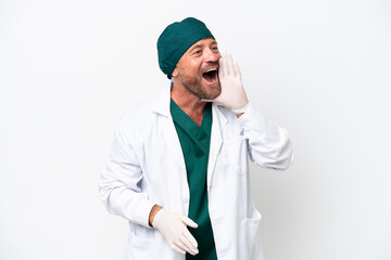 Middle age surgeon in green uniform isolated on white background shouting with mouth wide open to...