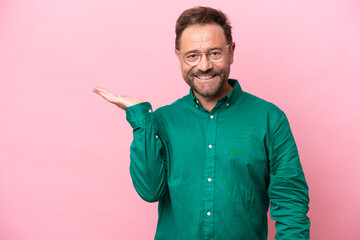 Middle age caucasian man isolated on pink background holding copyspace imaginary on the palm to...