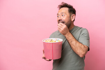 Middle age caucasian man isolated on pink background holding a big bucket of popcorns