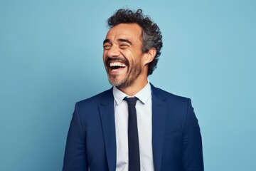 Handsome middle-aged man laughing and looking at camera against blue background
