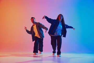 Talented male and female hip-hop dancers performing in synchronously moves against gradient studio background in neon light. Concept of youth culture, lifestyle, urban style, action. Gel portrait.