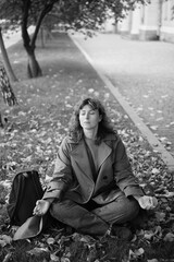 Caucasian middle aged woman meditating in lotus pose at autumn city street with leaves. Woman relaxing on yellow leaves. Meditation, Mental health, self care, mindfulness. High quality photo