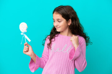 Little caucasian girl holding a lollipop isolated on blue background celebrating a victory