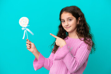 Little caucasian girl holding a lollipop isolated on blue background and pointing it