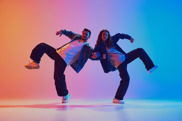 Dynamic portrait of dance duo, talented man and woman in dance poses against gradient studio background in neon light, filter. Concept of youth culture, music, lifestyle, hobby, action. Gel portrait.