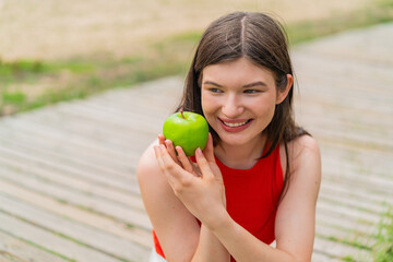 Young pretty woman at outdoors holding an apple with happy expression