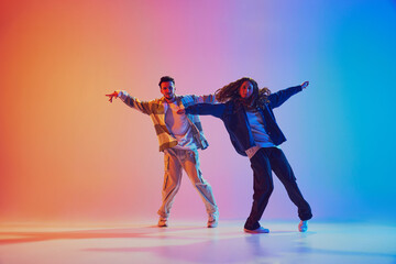 Dynamic photo of two fashion dressed people, dancing in motion against gradient studio background...