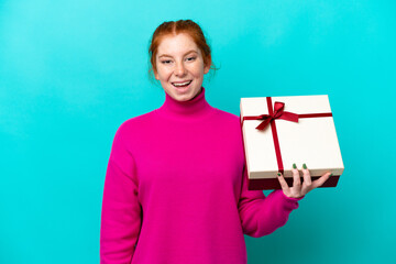 Young caucasian reddish woman holding a gift isolated on blue background with surprise and shocked...