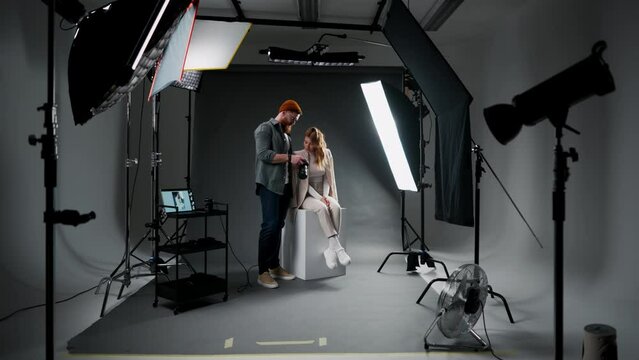 Bearded man making pictures of female model against black background and octabox in professional studio