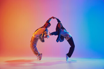 Dynamic shot of young dance duo holding hands while dancing in motion against gradient background in neon light. Concept of youth culture, music, lifestyle, style and fashion, action. Gel portrait. - obrazy, fototapety, plakaty