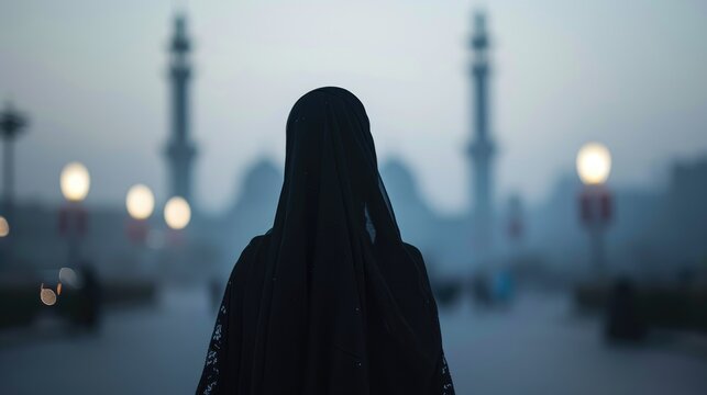 A Muslim woman in a niqab walking towards a big mosque, her figure silhouetted against the evening lights, back view