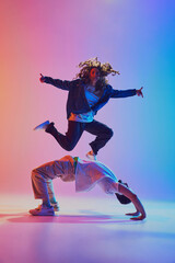 Acrobatic dance pair, woman jumping and man in handstand, against gradient studio background in neon light, filter. Concept of youth culture, music, lifestyle, style and fashion, action. Gel portrait.