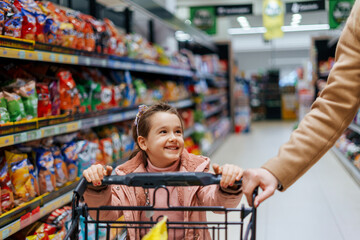 Mother and daughter enjoy moments together in the store. A child stands on a shopping cart while...