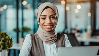  happy muslim businesswoman in hijab at office workplace. Smiling Arabic woman working on laptop in a modern office