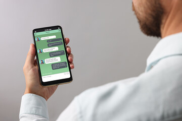 Man texting with friend using messaging application on smartphone against grey background, closeup
